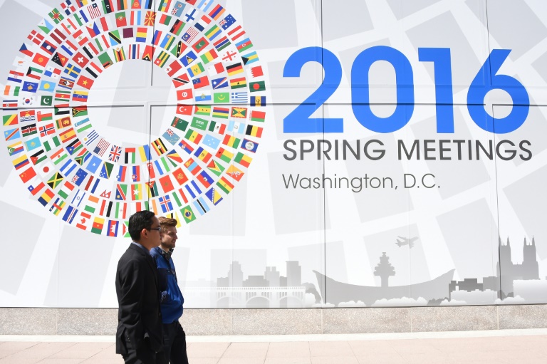 Deux hommes passent devant un panneau annon&ccedil;ant le meeting du monde de la finance &agrave; Washington, le 13 avril 2016. &copy; AFP